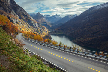 View of a road going uphill along the Geiranger fjord in Norway with town of Geiranger in the...