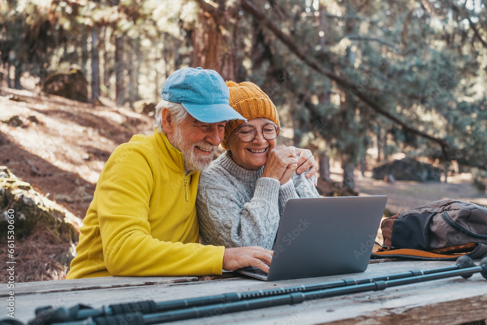 Sticker Head shot portrait close up of cute couple of old middle age people using computer pc outdoors sitting at a wooden table in the forest of mountain in nature with trees around them..