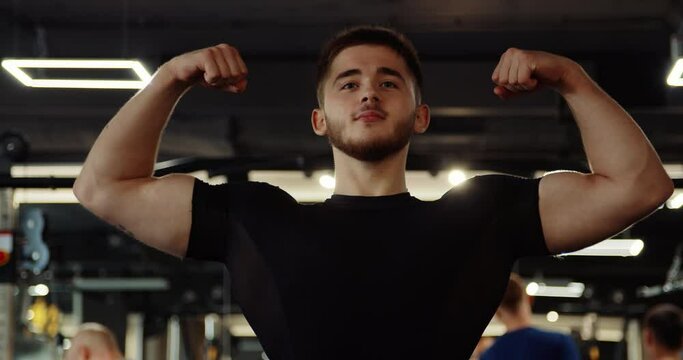 Medium shot of athletic handsome young man performing bench press in gym. Man wears black long sleeve compression shirt, blue shorts. Facial muscles work. High quality 4k footage
