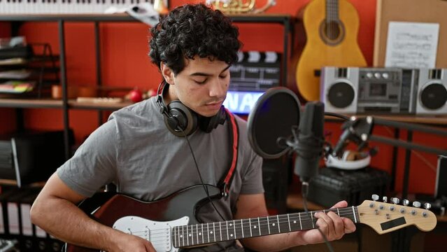 Young latin man musician composing song playing electrical guitar at music studio