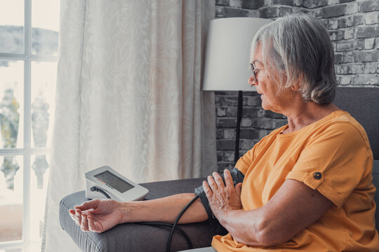 Senior Elder Woman Measure High Low Blood Pressure Test Holding Using Medical Digital Electronic Meter Sit On Sofa At Home, Heart Disease Atherosclerosis Prevention, Hypotension Hypertension Concept.