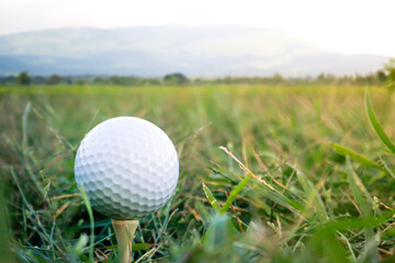 A golf ball is placed on the grass with a mountain view behind.
