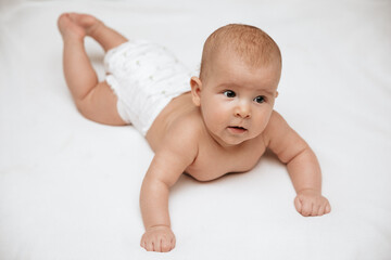 A newborn baby in a diaper is lying on stomach on a white background and looking to the side.