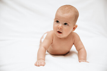 A surprised newborn baby in a diaper is lying on a white blanket and looking. 