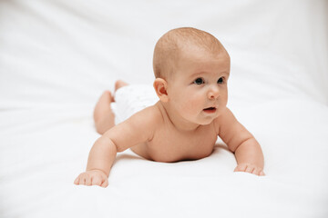 A newborn baby in a diaper is lying on stomach on a white background and looking to the side.