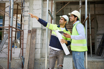 workers or architects meeting and pointing up to something at construction site