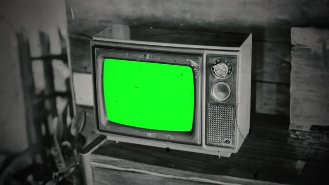 Old Broken TV Green Screen Vintage Television Film Effect Zoom In. Old retro television with green screen on the table of a wooden house, film texture. Zoom in
