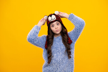 Modern teenage girl 12, 13, 14 year old wearing sweater and knitted hat on isolated yellow background. Funny face.