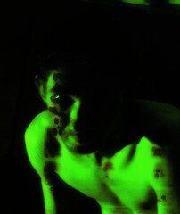 Portrait, digital collage, special processing. Dark, scary, shirtless man looking. Mainly green.