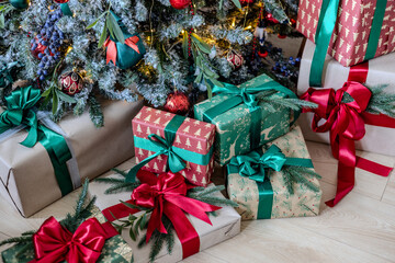 A variety of colored Christmas gifts stand near a decorative Christmas tree in the house on the floor under the branches.