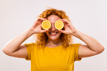 Happy ginger woman is covering her eyes with slices of lemon.