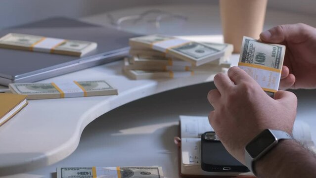 Close-up of American US dollars in hands, counting money. Business person sitting at the table, counts earned money, fixing profits. Business man calculates 100 usd banknotes in hands