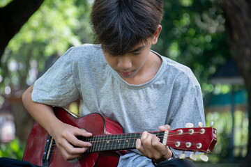 Asian cute boy playing guitar in the front yard of his own house happily, soft focus, concept for recreational activity and free times hobbies of children around the world. - obrazy, fototapety, plakaty