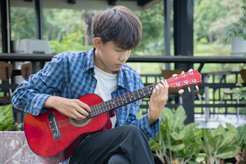 Asian cute boy playing guitar in the front yard of his own house happily, soft focus, concept for...
