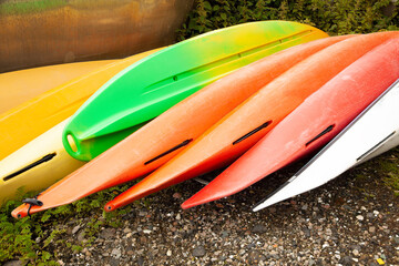 varios kayacs  invertidos  de varios colores, rojos naranja, verde, amarillo reposando en la arena de la playa - obrazy, fototapety, plakaty