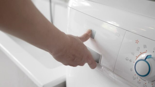 A woman pours a laundry conditioner into the liquid detergent compartment of a home washing machine and closes the powder container