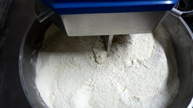 Baker knead the dough for bread in a dough mixer in an industrial bakery. Production of bakery products.