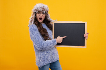 Teenage girl kid hold in warm hat hold blackboard chalkboard with copy space on yellow background....