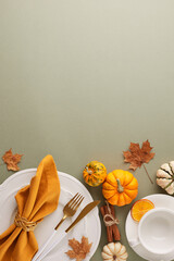 Forge a memorable Thanksgiving table. Top view vertical photo of plates, cutlery, pumpkins, napkin, cup, dry orange slices, cinnamon, autumn leaves on light green background with promo area