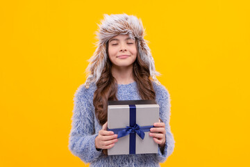 happy kid long hair in hat with gift box making wish on yellow background, anniversary