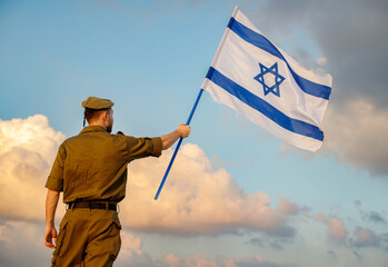 A guy in a soldier's uniform with an Israeli flag in his hand against a cloudy sky. Remembrance Day - Yom HaZikaron, Patriotic holiday, Israeli Independence Day - Yom Ha'atzmaut concept.