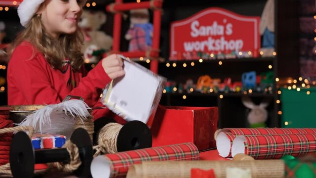 Little Santa helper putting stuffed toy into gift box at workshop, slow motion, putting stuffed toy into a box at toy factory of Santa Claus
