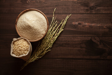Organic whole Rice (Oryza sativa) in a jute bag. Rice Bran, and Rice Flour in a wooden bowl, isolated on a dark wooden background. Top view.