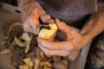Elderly woman's hands doing domestic work of peeling potatoes. Aged hands with joint problems, osteoarthritis. Concept of active aging despite associated diseases. Close up