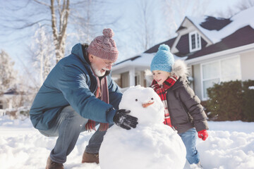 A girl has fun with her grandfather building a snowman on a sunny winter day near the house, outdoors