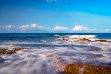 Sea waves break on the stone coast and foam between the rocks.