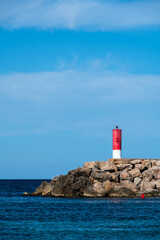 A lighthouse on the rocks reaching into the sea on a beautiful sunny day.