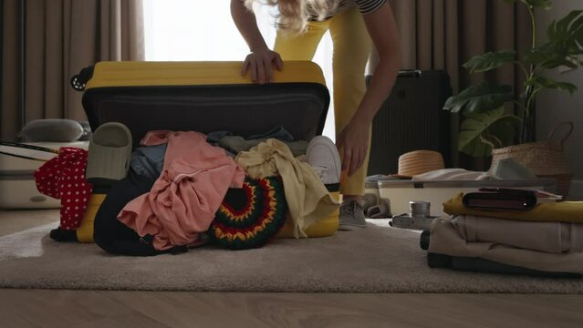 Woman randomly chaotic packs clothes into suitcase. Spontaneous woman throwing clothes into suitcase oblivious to order or planning. Woman not know how to pack clothes correctly in organized manner