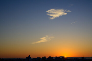 都市の夜明け。日の出とともに空と雲がオレンジ色に染まり、ビル群はシルエットとして写す。神戸市東灘区から大阪方面をのぞむ