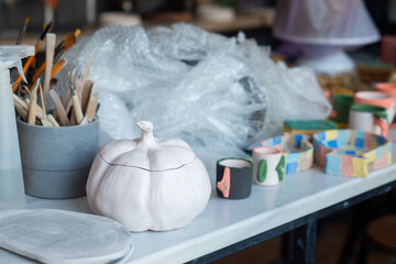 Table cluttered with various unfinished Halloween crafts at a ceramics, pottery studio with tools,...