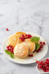 Cottage cheese pancakes, syrniki, ricotta fritters with fresh berries and sour cream on white marble background close up. Healthy and delicious breakfast, high key text space
