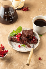 Two pieces of chocolate cake brownie decorated with red currant berries and mint for coffee on beige textured background
