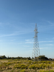 Overhead line pylons, high voltage pylons in meadow with mountains on background