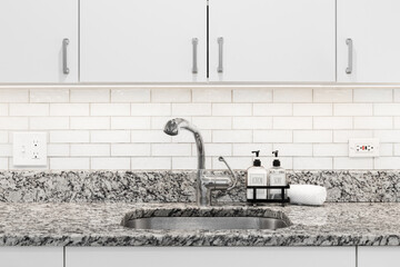 A kitchen sink detail with a chrome faucet, marble countertop, white cabinets with under cabinet...