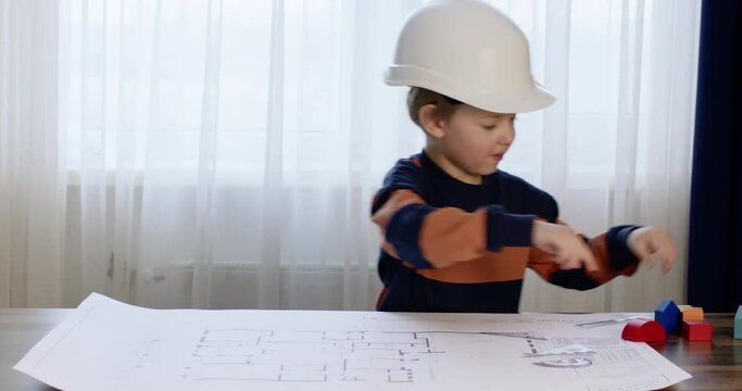 A child in a construction helmet plays builder, takes measurements using a ruler and puts wooden toy houses on the drawing.