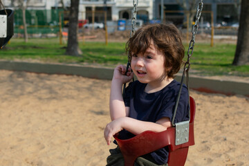 A little boy sitting on the swing in the playground looking away