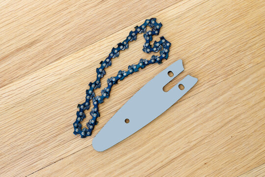 The metal chain and bar for the saw on the wooden table before installation or replacement.