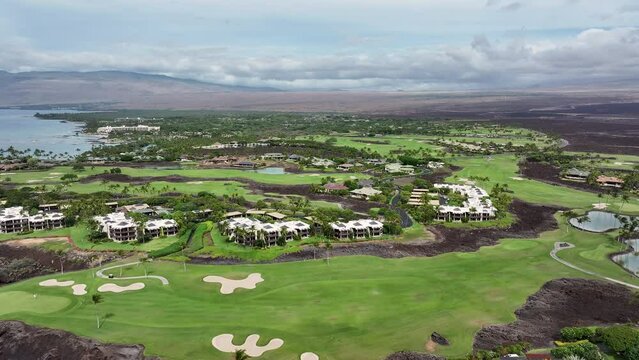 Aerial ocean bay golf luxury homes Kona Hawaii pull fast. Luxury exclusive homes on coast golf course. Economy is tourism based. Volcanic lava rock black sand beach. Water tropical beach recreation.