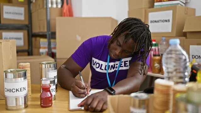 African american man volunteer checking products writing on clipboard at charity center