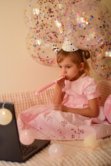 Fototapeta premium Birthday online. Child celebrates birthday by laptop. A little girl celebrates her birthday with her parents, relatives and friends via video call. Holiday in isolation. Little princess