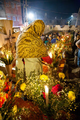 Día de muertos, mujer orando hacia un camino de tumbas en Mixquic.