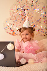 Fototapeta premium Birthday online. Child celebrates birthday by laptop. A little girl celebrates her birthday with her parents, relatives and friends via video call. Holiday in isolation. Little princess