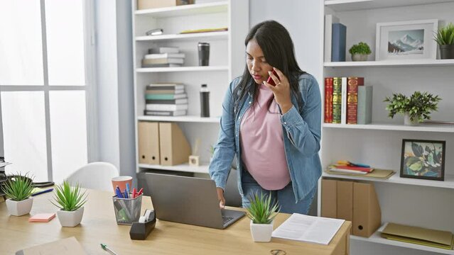 Expecting young woman worker bossing business, relaxed at the office, talking on smartphone, laptop within reach.