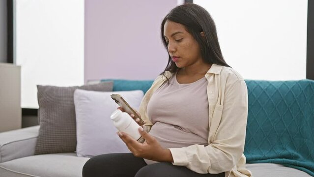 Worried young hispanic woman, pregnant and ill, glued to her smartphone at home, nervously consulting pill information