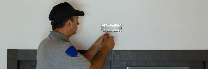 Image of an electrician on a ladder installing emergency lights in a house. Do-it-yourself energy...