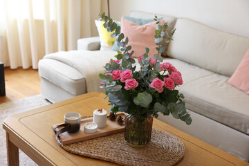 Beautiful bouquet of roses and eucalyptus branches in vase near candles on table in room